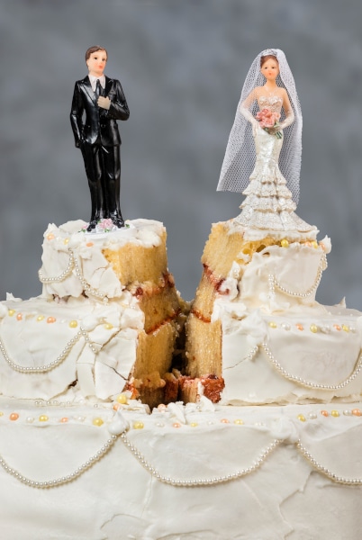 A wedding cake split down the middle with a model Bride on one side and a model Groom on the other signifying divorce and separation