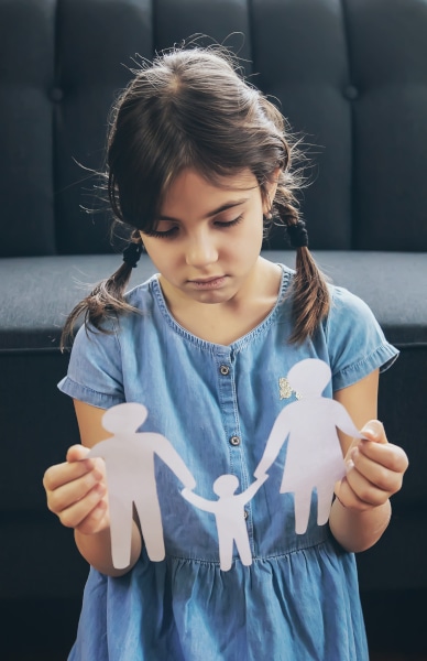 A little girl with pigtails in a blue dress holds a paper cutout of a family, as the parents argue about residence and contact