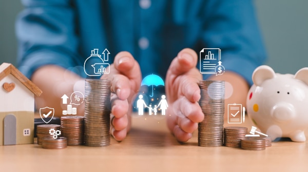 Man's hands separating piles of coins with models house on one side and a piggy bank on the other overprinted with financial symbols