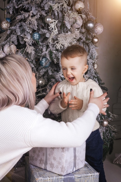 Mother lifting a happy baby in front of a Christmas Tree as a result of arranging co-parenting at Christmas Scotland