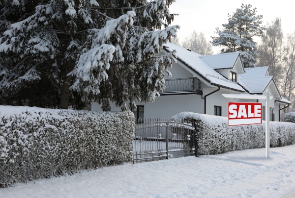 House for sale over Christmas with snow on the ground and a for sale sign in front of it