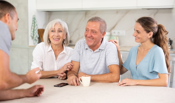 Older parent and adult children talking around a kitchen table about family matters.