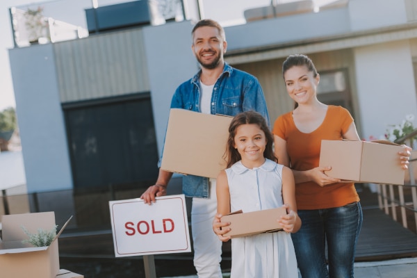 Family beside a For Sale sign as they sell their old home to reclaim the Additional Dwelling Supplement